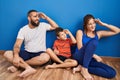 Family of three sitting on the floor at home very happy and smiling looking far away with hand over head Royalty Free Stock Photo