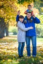 Family of three walks in the autumn park holding hands. happy father carrying son with maple leaves. Mother embrace her cute boy Royalty Free Stock Photo