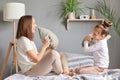 Family time on weekend. Young mother and her little daughter playing in bed, funny pillow fight, enjoying the moment, having fun Royalty Free Stock Photo