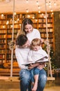 Family togetherness. Mom, dad and son reading story book together sitting on swing evening home. Family and Parenthood Concept. Royalty Free Stock Photo