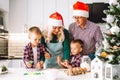 Family of two twins boys and age parents preparing cookies for Christmas ot New Year in light kitchen wearing Santa hats.