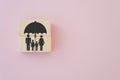Family under umbrella icon on wooden cube block with sweet pink background for life, family, group insurance concept with copy