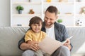 Family and upbringing concept. Happy little boy enjoying storytelling time with his daddy, sitting with big book