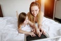 Family using laptop laying on white bed woman and kid girl daughter with sunshine Royalty Free Stock Photo