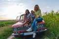 Family vacation, mom with theyr teen children all in casual clothes sitting together on a hood of the retro car among