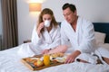 Young couple in bathrobes having a breakfast together in bed in hotel room. Royalty Free Stock Photo