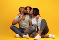 Family values concept. Young african american parents kissing cheeks of their daughter, sitting on yellow background Royalty Free Stock Photo