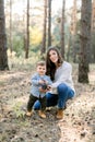 Family walk in the autumn forest. Attractive young mother and her little son playing together with pine cones, posing to Royalty Free Stock Photo