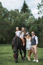 Family walk, horse riding concept. Two little girls riding a brown horse, while young stylish parents in casual cowboy Royalty Free Stock Photo