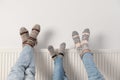 Family warming legs on heating radiator near white wall, closeup