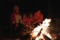 Family warms near campfire in forest and having a conversation. Night camping near bonfire in pine forest. Tourism and camping