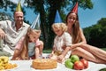 Family wearing party hats, enjoying celebrating kids birthday in the park on a summer day