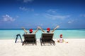 A family wearing santa claus hats sits in sunbeds on a tropical beach Royalty Free Stock Photo