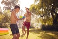 Family Wearing Swimming Costumes Having Water Fight With Water Pistols In Summer Garden