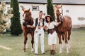 A family in white clothes with their son stand near two beautiful horses in nature. A stylish couple with a child are photographed