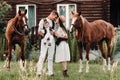 A family in white clothes with their son stand near two beautiful horses in nature. A stylish couple with a child are photographed