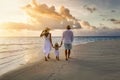 A family in white summer clothing walks hand in hand down a tropical paradise beach during sunset tme Royalty Free Stock Photo