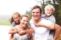 A family who plays together. Happy young parents piggybacking their children and smiling while outdoors - portrait. Royalty Free Stock Photo