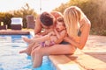 Family With Young Son Sitting On Edge Of Pool Having Fun On Summer Vacation In Outdoor Swimming Pool Royalty Free Stock Photo