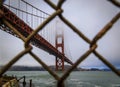 The famous Golden Gate bridge viewed through a rusty chain link fence on a cloudy day in San Francisco, California Royalty Free Stock Photo