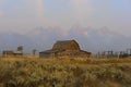 The famous John Moulton Barn within Mormon Row in Wyoming with mountains and clouds in the background.