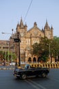 Famous Mumbai yellow-black taxi car and at background Chhatrapati Shivaji Terminus (CST) is a UNESCO World Heritage Site and an h