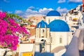 Famous Santorini view. Three blue domes and traditional white houses with bougainvillea flowers. Oia village, Santorini island,