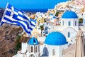 Famous Santorini view. Three blue domes and traditional white houses with Greek flag. Oia village, Santorini island, Greece Royalty Free Stock Photo