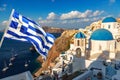 Famous Santorini view. Three blue domes and traditional white houses with Greek flag. Oia village, Santorini island, Greece Royalty Free Stock Photo