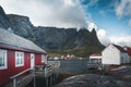 Famous tourist attraction of Reine in Lofoten, Norway with red rorbu houses, clouds, rainy day with bridge and grass and Royalty Free Stock Photo