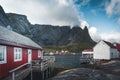 Famous tourist attraction of Reine in Lofoten, Norway with red rorbu houses, clouds, rainy day with bridge and grass and