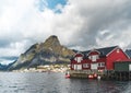 Famous tourist attraction of Reine in Lofoten, Norway with red rorbu houses, clouds, rainy day with bridge and grass and Royalty Free Stock Photo