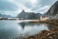 Famous tourist attraction of Reine in Lofoten, Norway with red rorbu houses, clouds, rainy day with bridge and grass and