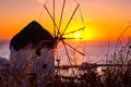 Famous traditional Greek windmill, Mykonos, Greece against sunset. Beautiful sky, sun touch sea horizon, high grass in Royalty Free Stock Photo