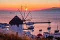 Famous traditional Greek windmill over port of Mykonos, Greece at sunset. Beautiful sky, sun touch sea horizon, boats Royalty Free Stock Photo