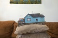 A fanciful photograph of a miniature cottage on some pillows on a couch