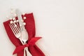 Fancy Christmas Table Place Setting with red napkin, silverware, and white berries on creamy white tablecloth background with copy