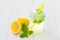 Fancy cool glass of lemonade with ice and mint, Mason jar style cup with yellow straw, green leaves of fresh mint and lemons, one