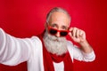 Fancy grey haired santa man making self photos wear sun specs knitted jumper isolated red background