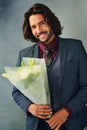 Fancy some romance. Studio portrait of a stylishly dressed handsome young man smiling and holding a bouquet of flowers.