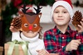 Fanny kids girl in deer mask and boy in Santa cap holding a cones in a hands