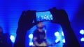 Fans hands recording video with smart phones at rock concert in beautiful blue colors on the background