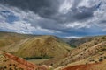 Fantastic deserted landscape. Multi-colored mountains against the sky covered by clouds with sun rays. Red and brown hills. Altai