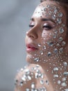 Fantastic fashion portrait of a young beautiful woman with transparent crystals on her face and shoulders.