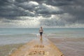 Fantastic image of a man in a white shirt and shorts coming from the sea on a cement pier on a dark sky day with early rainy Royalty Free Stock Photo