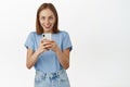 Fantastic offers at online store. Excited young woman using smartphone, looking amazed and happy, found shopping app on Royalty Free Stock Photo