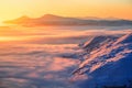 Fantastic scenery with the high mountains in snow, dense textured fog and a sunrise in the cold winter day.