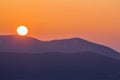 Fantastic wide panorama view of big bright white sun in dramatic orange sky over dark purple mountain range at sunset or sunrise i Royalty Free Stock Photo