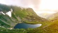 Fantastic wide peaceful view of blue lake in green valley and small tourist tents at rocky mountain with patches of snow covered Royalty Free Stock Photo