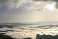 Fantastic wide top view of mountain valley filled with white puffy like snow clouds and fog stretching to horizon under bright mor Royalty Free Stock Photo